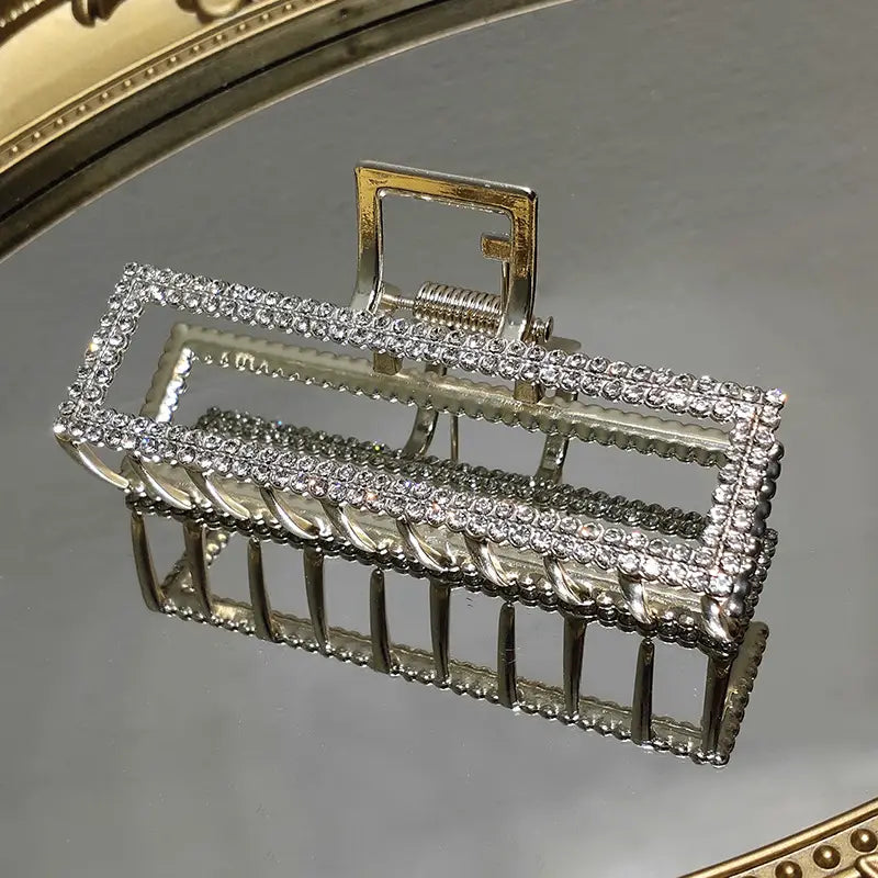 An elegant sweet pearl silver claw clip featuring a sparkling silver frame adorned with clear rhinestones and decorative metal bars.