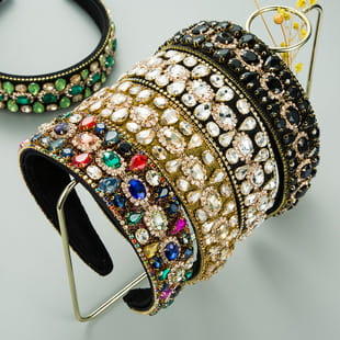 A collection of baroque colorful headbands featuring ornate wide designs adorned with sparkling gemstones in various vibrant colors and metallic finishes.