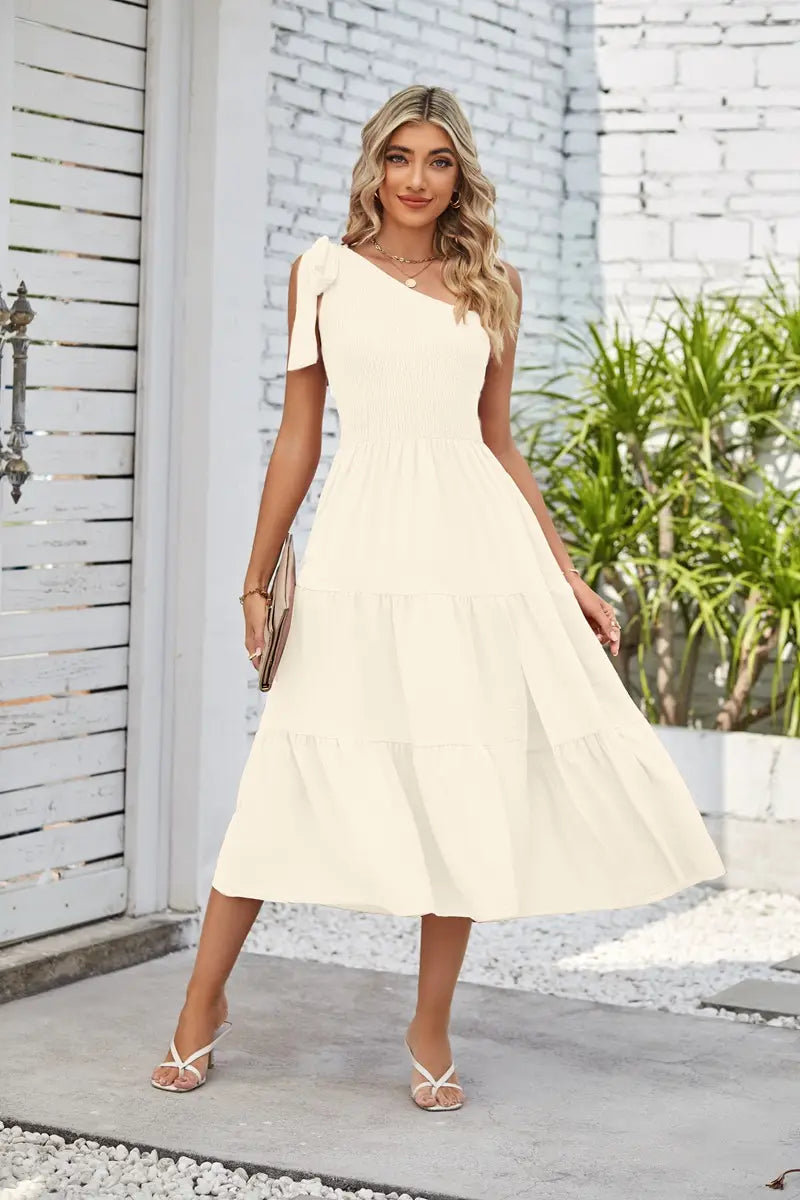 A flowing off-the-shoulder cream midi dress with tiered ruffles and a fitted bodice featuring a pleated layered hem and a layered hem split.