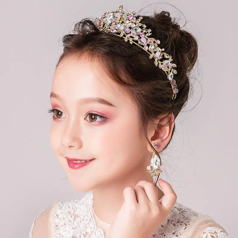 A delicate gold-toned princess crown tiara adorned with sparkling clear and soft pink crystals featuring an intricate floral design perfect for a cute princess crown or catwalk cute princess look.