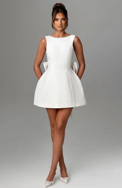 a sleek white sleeveless backless dress summer slim mini dress with a flared skirt and decorative bow accents at the waist featuring pearl embellishments