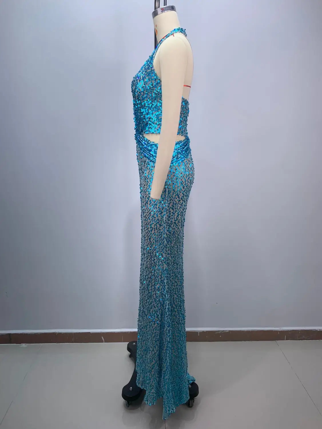 A shimmering turquoise sequined slimming party stage host mermaid gown with a halter neckline and side cutouts displayed on a mannequin.