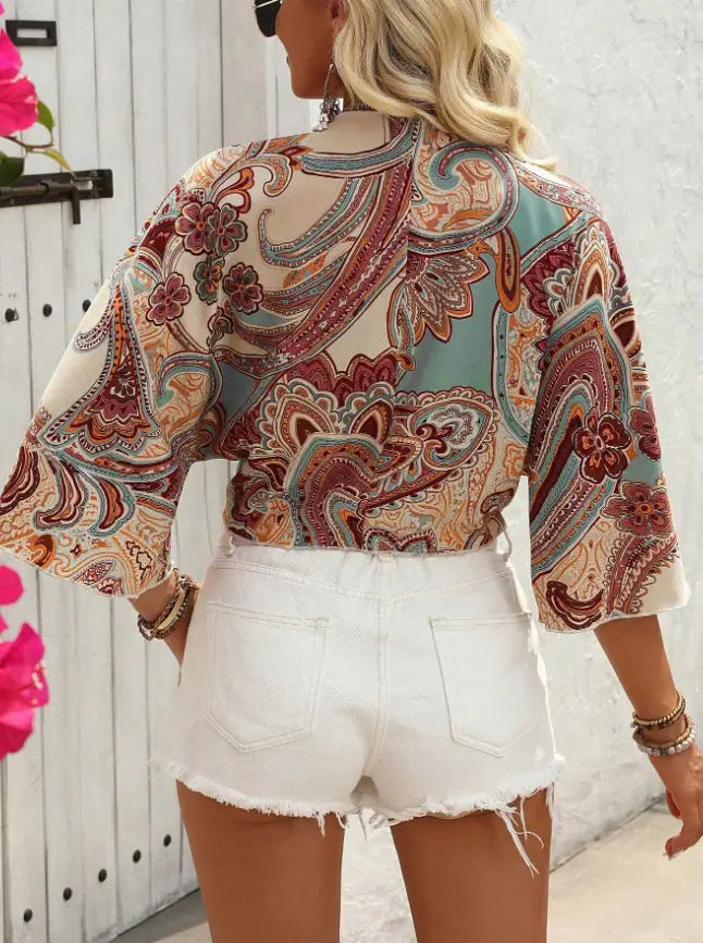 a woman wears a bohemian style printed front tie crop top featuring a vibrant paisley pattern in shades of red teal and beige with long sleeves