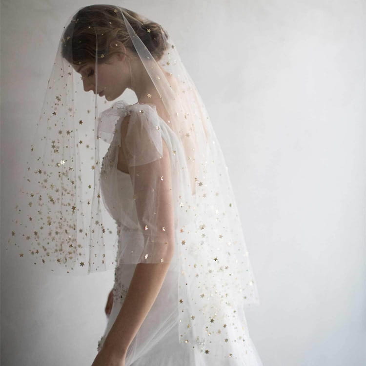 A delicate golden shiny big veil made of white tulle adorned with scattered silver star sequins.