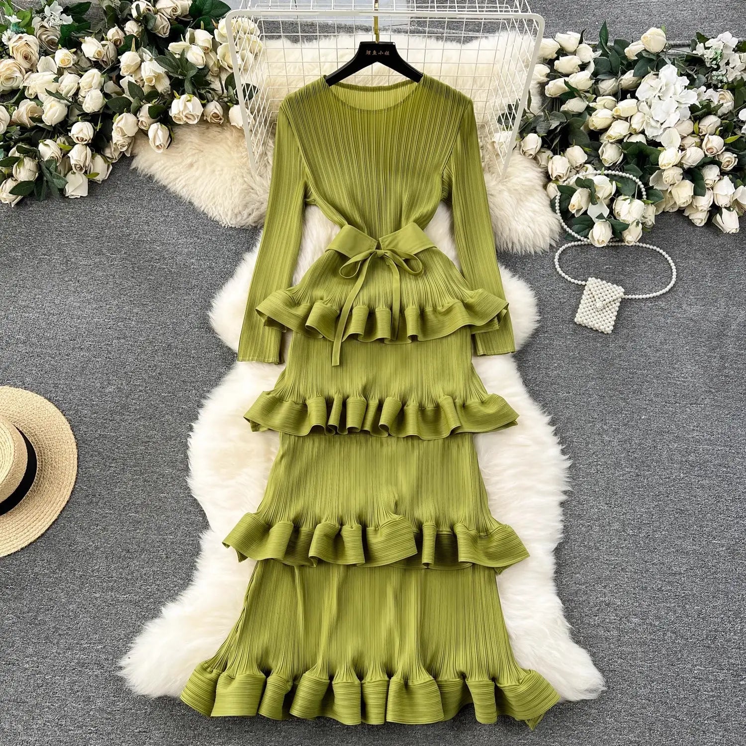 a long-sleeved olive green cake heavy industry pleated long dress with tiered ruffles and a matching belt designed for a slim fit silhouette