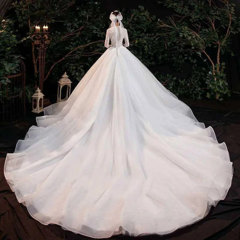 Elegant lace bridal gown with intricate lace detailing, long sleeves, and a voluminous white tulle skirt back view