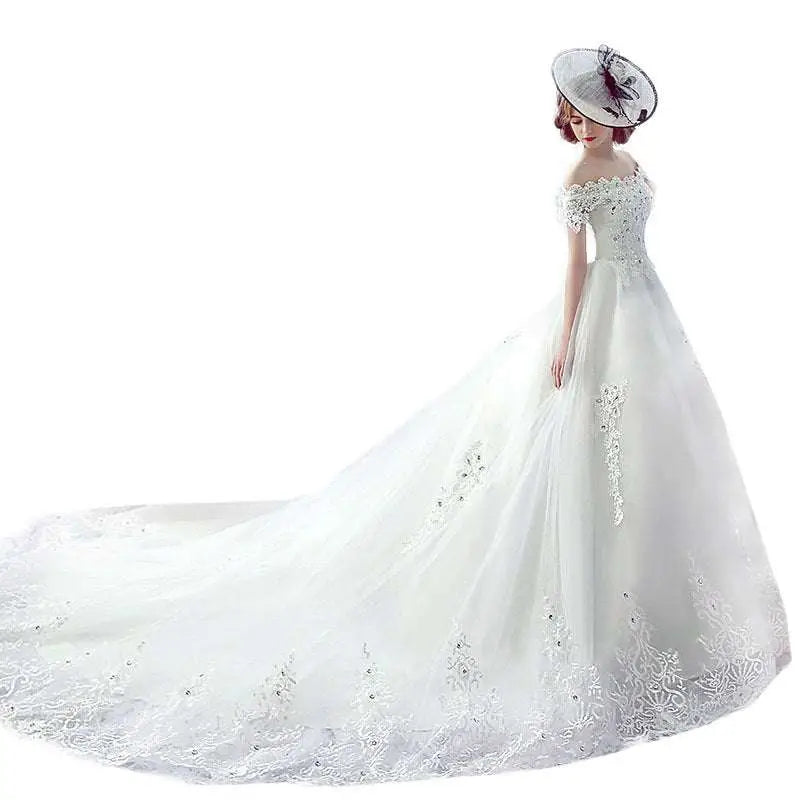 White off-the-shoulder wedding dress with intricate lace detailing and a flowing tulle skirt featuring a trailing french veil