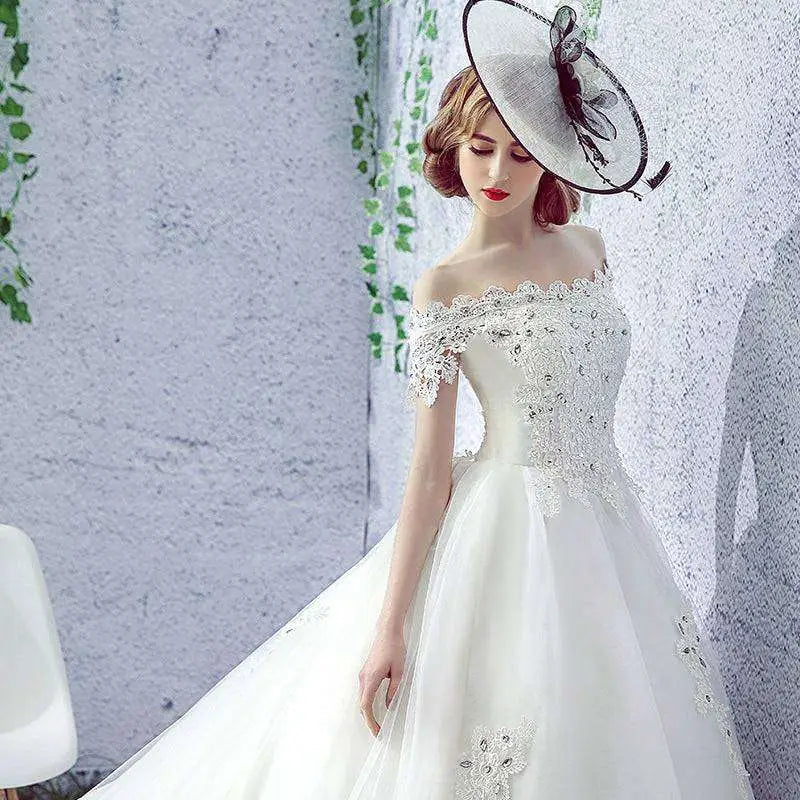 Elegant off-the-shoulder white wedding dress with intricate lace and beaded detailing paired with matching fascinator hat