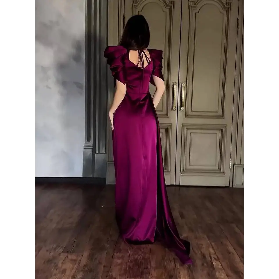A woman wearing an elegant puff sleeve pleated slit magenta maxi dress in deep satin fabric with a back tie detail