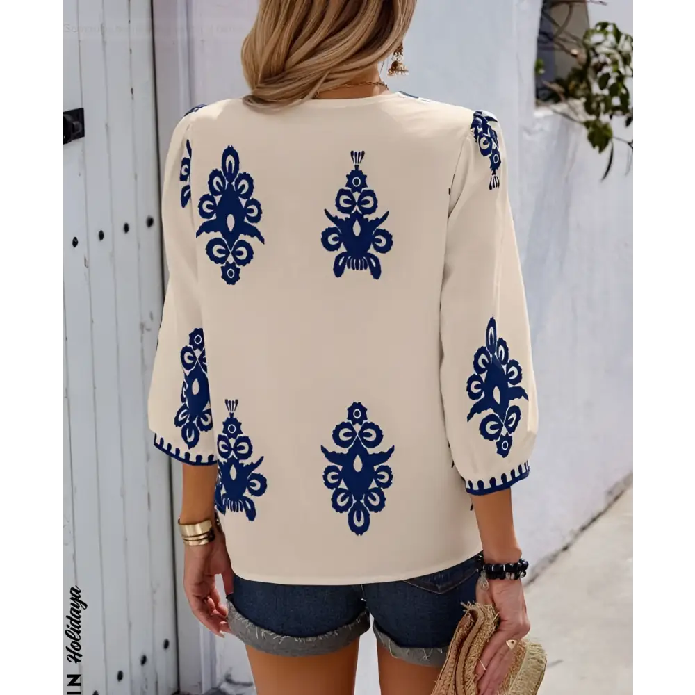Back view of cream-colored embroidered casual vacation blouse with navy blue embroidered floral patterns on sleeves and back