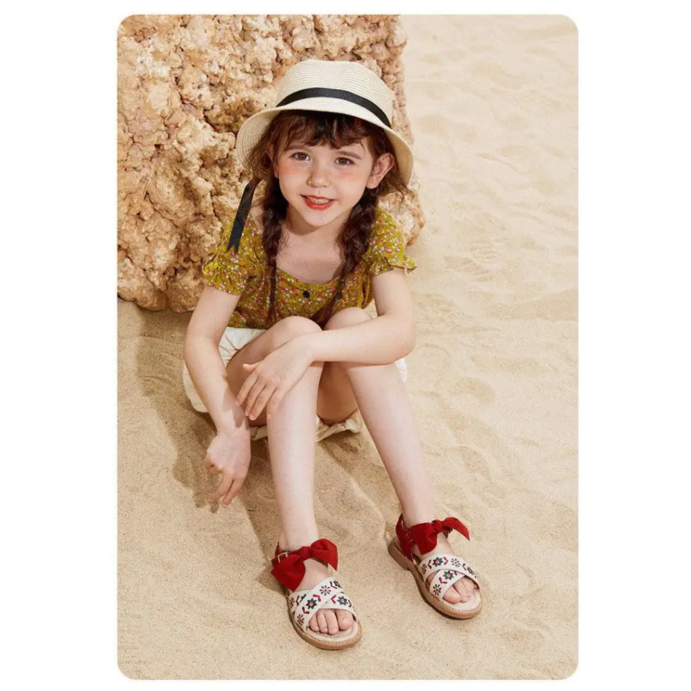 Beige children’s soft-soled sandals with black embroidered floral design and red bow accents for big kids