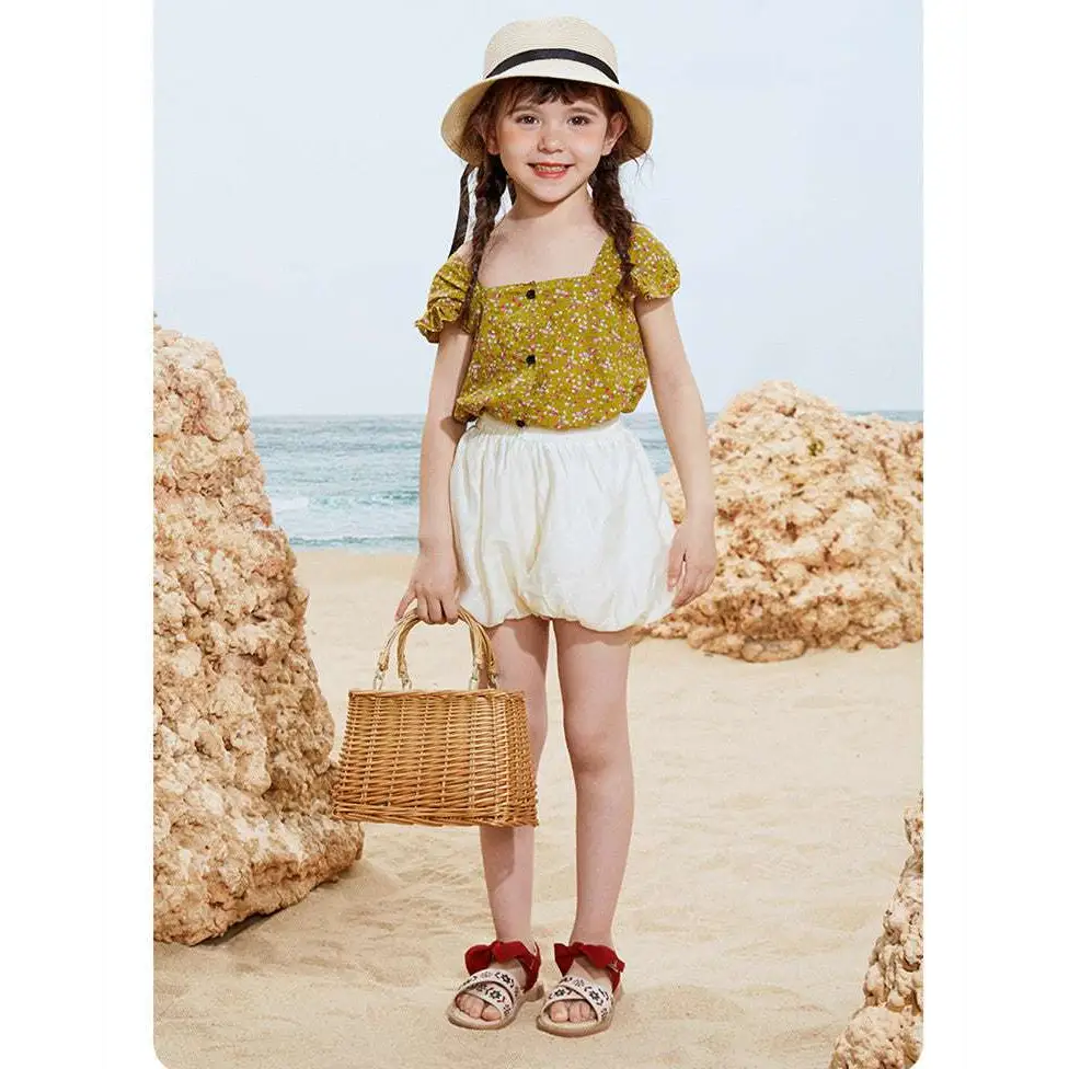 Woven wicker handbag with natural tan handles beside embroidered floral big children’s soft-soled sandals
