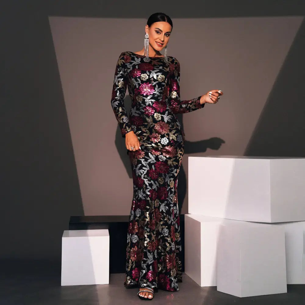A woman wears a black evening gown with embroidered floral patterns in burgundy pink silver and gold tones