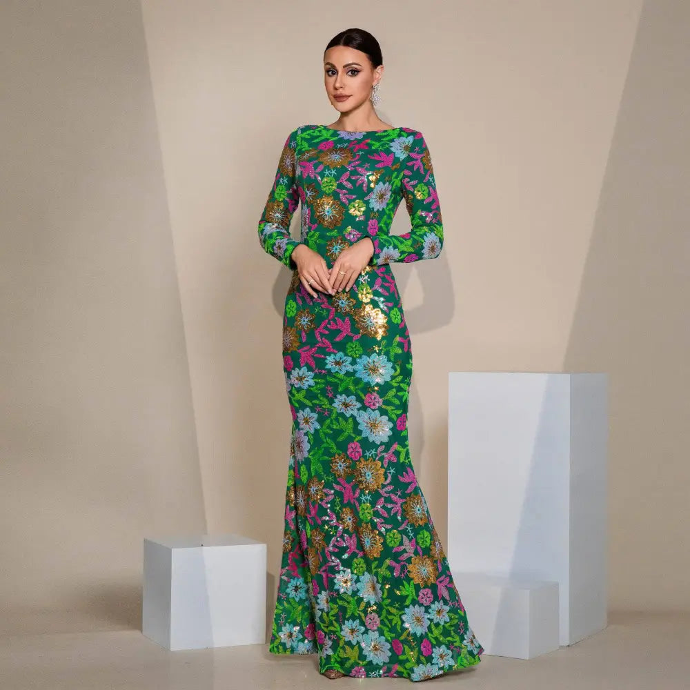 A vibrant emerald green evening gown featuring embroidered floral long sleeves with intricate pink blue and gold embroidery