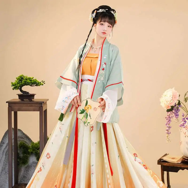 A woman wears embroidered han chinese clothing with floral embroidery in pastel hues and vibrant orange accents