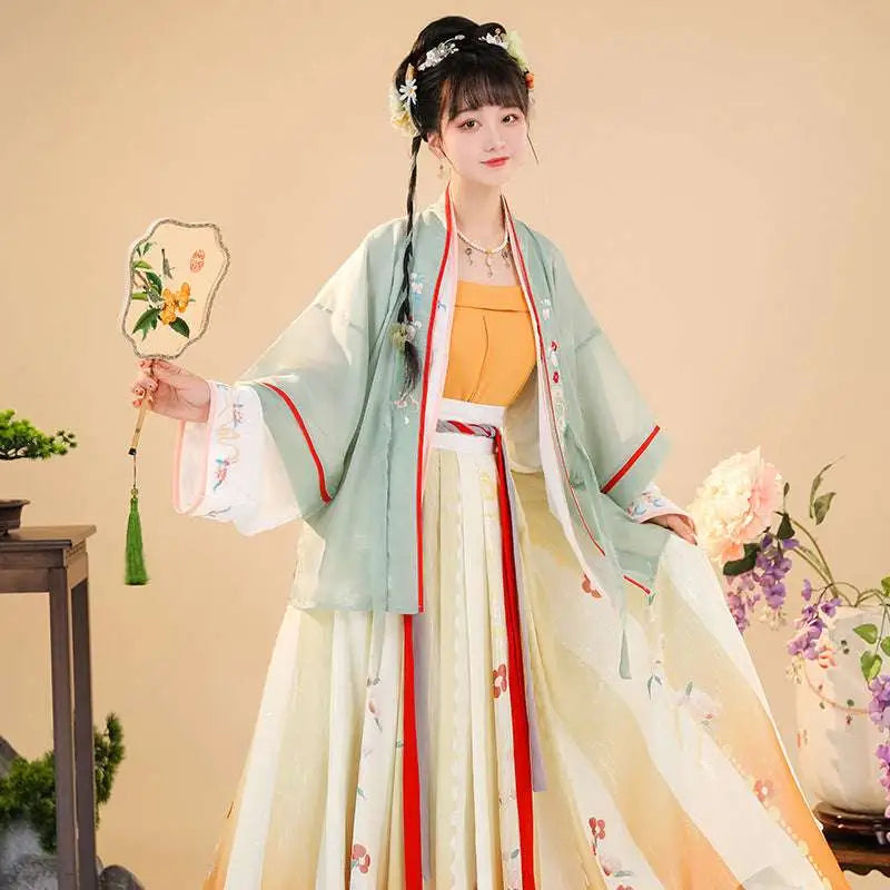 A woman wears embroidered han chinese clothing in light green and cream hanfu with red trim and floral embroidery details