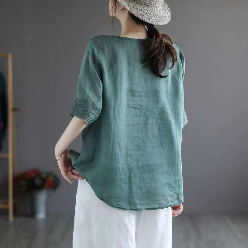 A soft teal cotton linen blouse with subtle embroidered detailing on the cuffs in fashion retro style