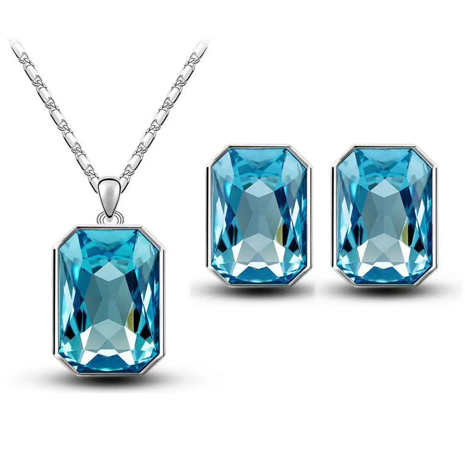 A pair of silver-toned earrings and matching crystal necklace pendant featuring radiant turquoise emerald green crystal stones