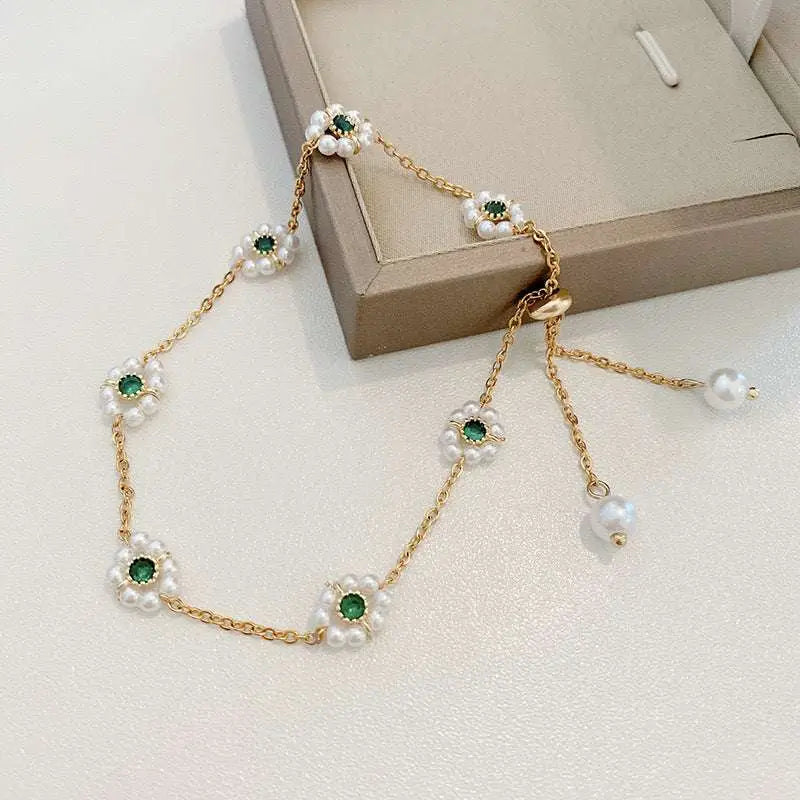Emerald pearl flowers bracelet featuring a delicate gold chain with white pearl flowers and green gemstones, adjustable chain
