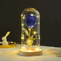 A sparkling deep blue eternal rose led with a golden stem in an elegant glass dome illuminated by warm fairy lights romantic gift