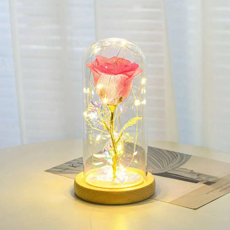 A pink preserved eternal rose led light with golden stem in an elegant glass dome and wooden base romantic gift set