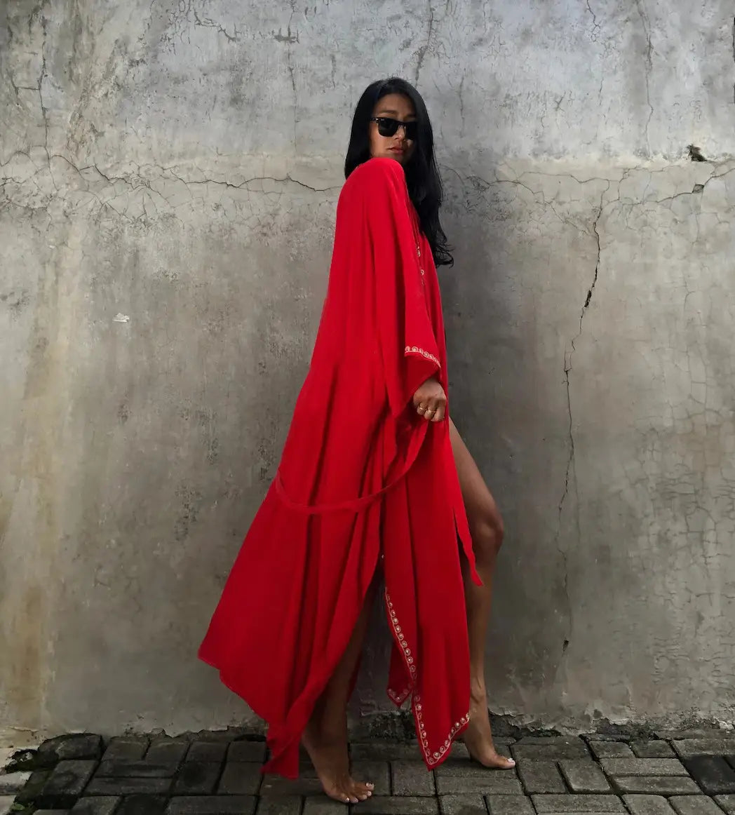 A flowing vibrant red rayon embroidered holiday maxi dress with delicate white embroidered trim along the hem and sleeves designed for holiday sun protection.