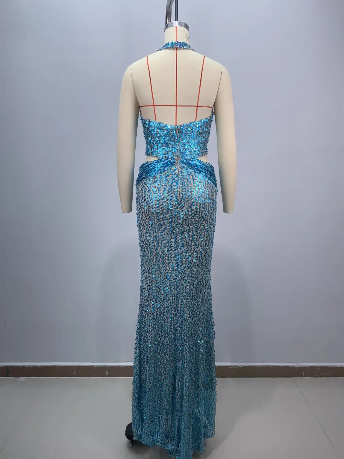 A shimmering turquoise sequined slim slimming party mermaid gown with a halter neckline and back cutouts displayed on a mannequin for party stage host use.