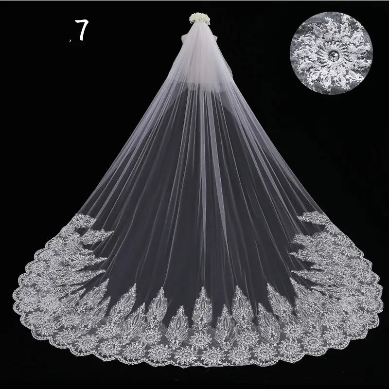 A delicate white lace wedding veil with intricate floral embroidery along scalloped edges and a small flower accent at the top in a long meters wide style.