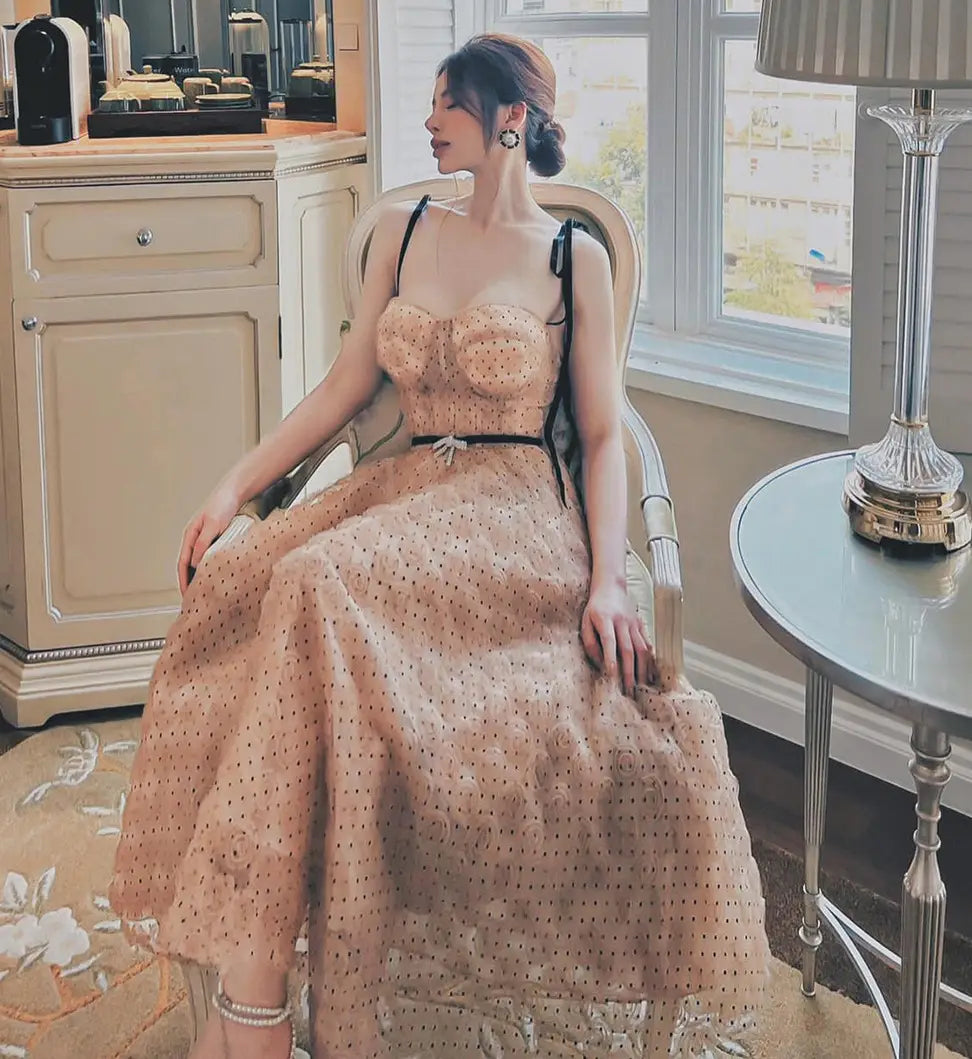 A woman wearing a blush pink slim drawstring dress made of sheer polka-dotted tulle with black straps and a matching belt.