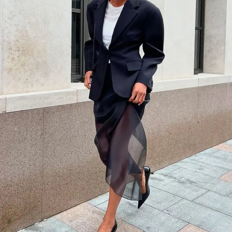 A black blazer with structured shoulders and tailored fit paired with a black sheer high waist slit sheath skirt featuring subtle geometric patterns.