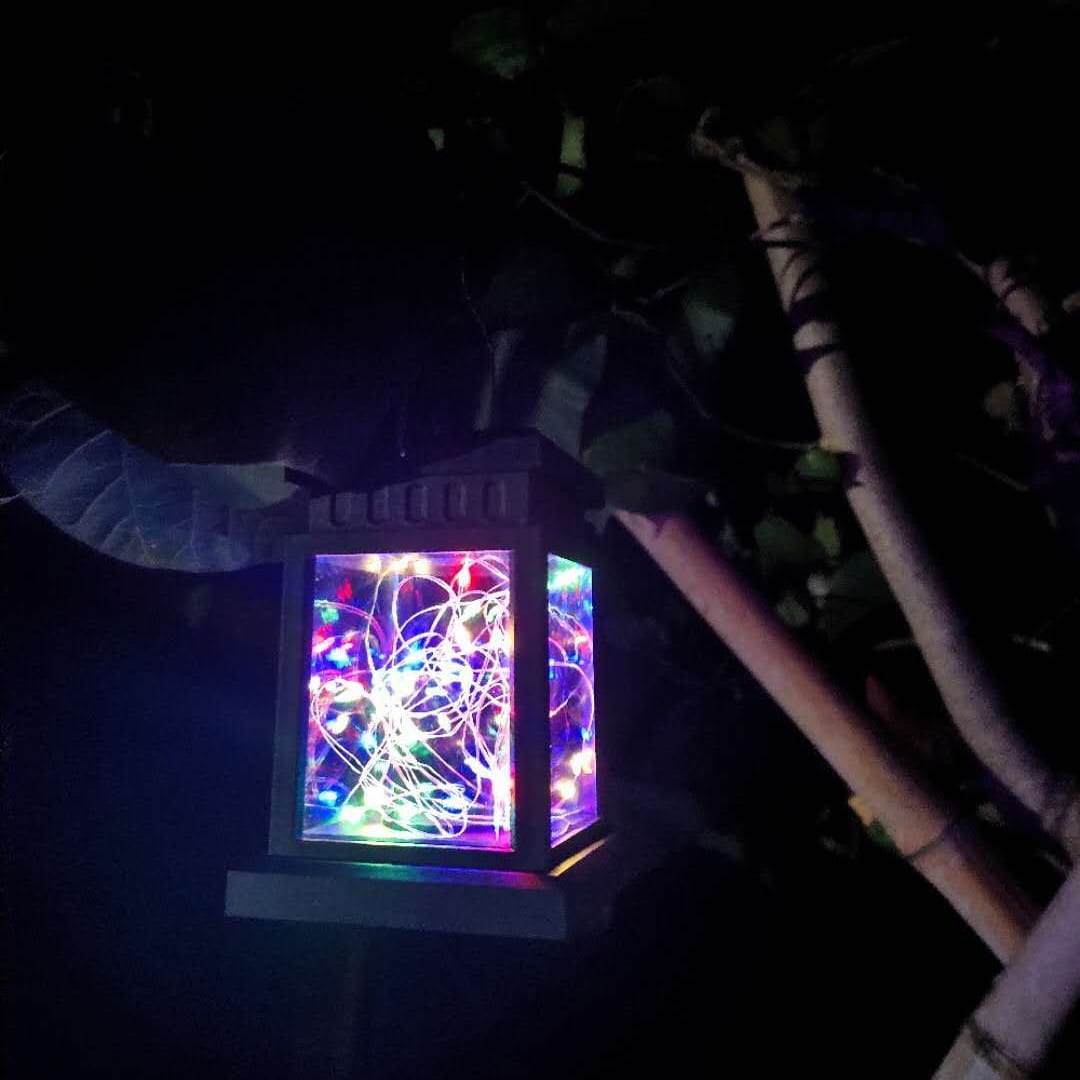 A glowing rectangular black solar waterproof garden hanging light with a dark frame and colorful LED lights swirling inside for outdoor waterproof garden use.