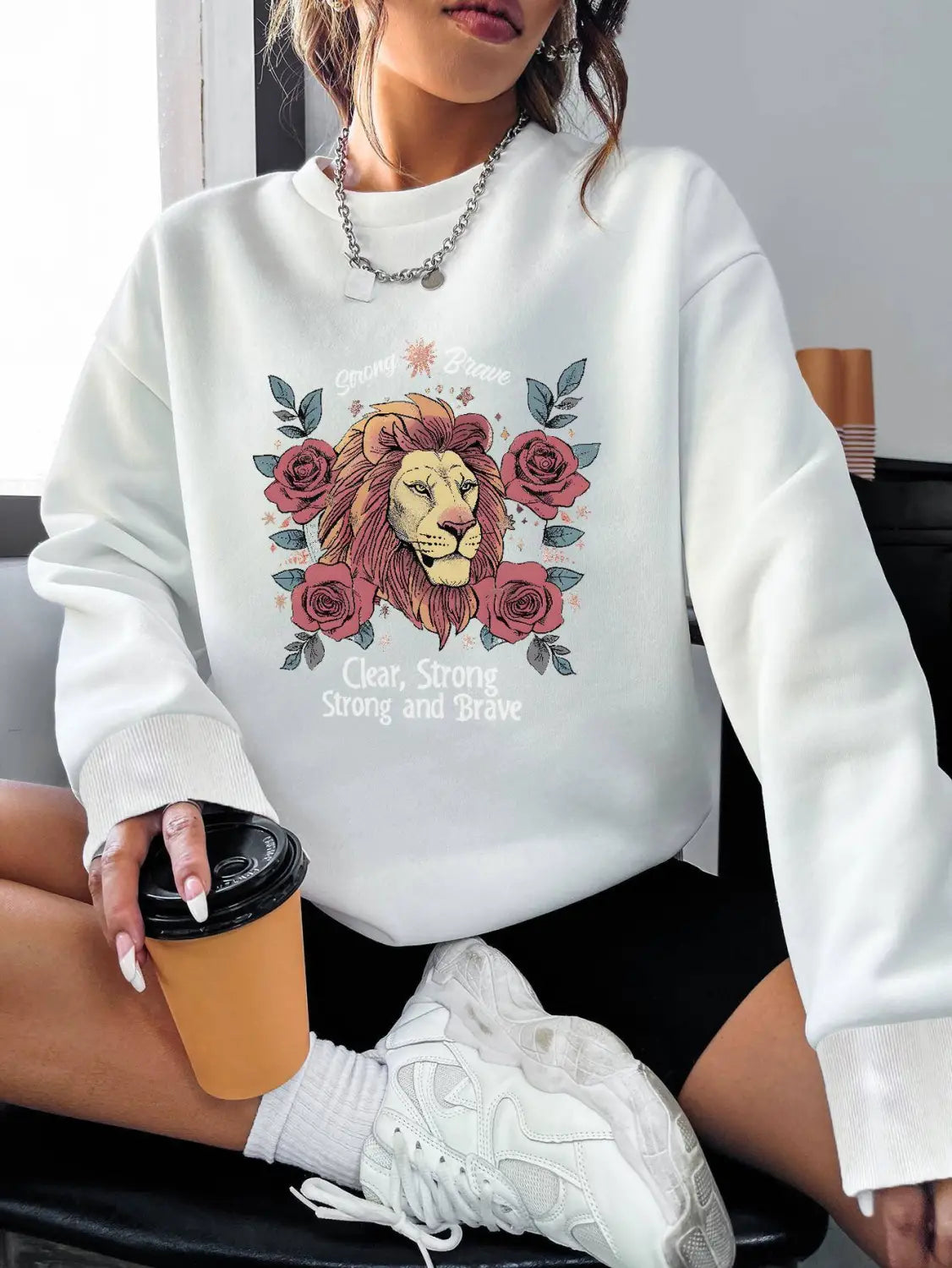 white regular fit long sleeve sweatshirt featuring a detailed embroidered lion surrounded by roses and the text clear strong strong and brave in an artistic design