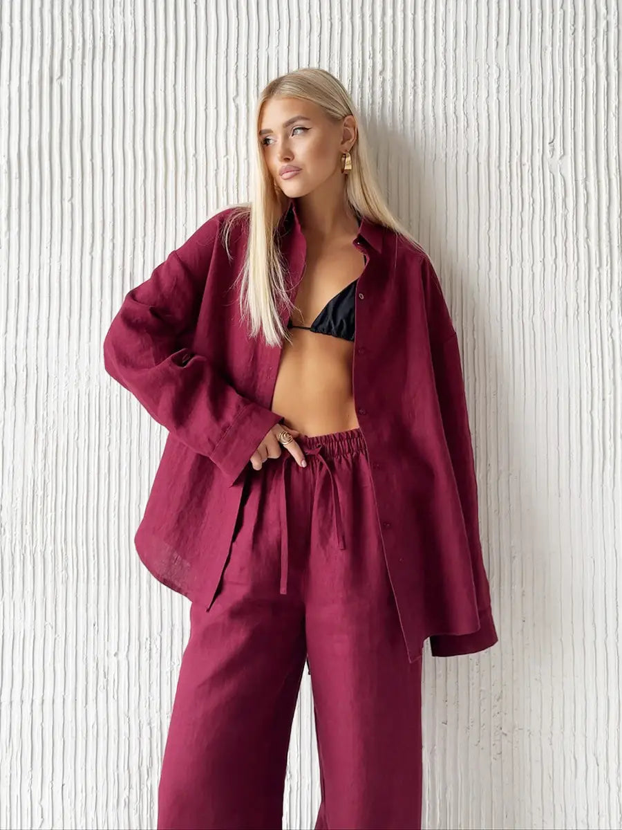 The model wears a loose-fitting maroon linen long sleeve shirt with an oversized silhouette and relaxed cuffs paired with a white linen cotton shirt trousers suit.