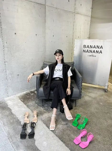 black high-waisted trousers with a sleek straight-leg cut and subtle side seam detailing paired with green minimalist square toe block heel sandals featuring a square toe design.