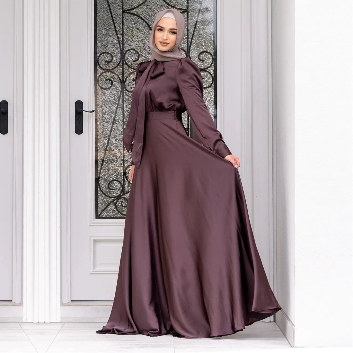 A flowing deep burgundy satin maxi dress with a fitted bodice long sleeves and a large hem satin design perfect for fashion large hem abaya styles.