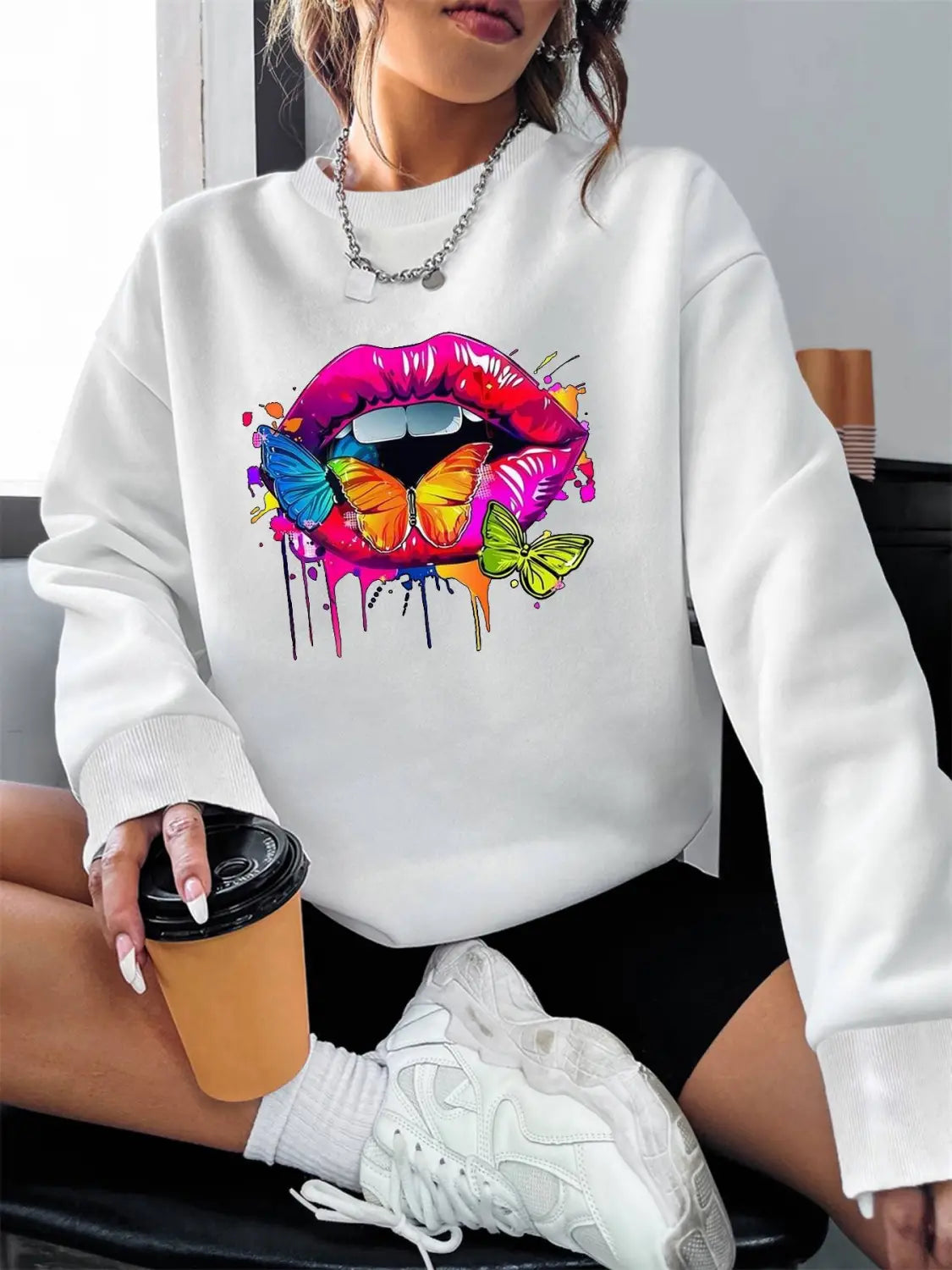 White crew neck sweatshirt featuring a vibrant colorful graphic of lips with butterflies and paint drips on the front.