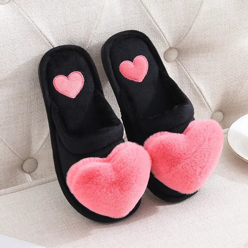 Black plush home slippers featuring fluffy pink heart accents on the front and embroidered hearts on the insole, ideal as cute love slippers for winter wear.