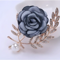 A delicate gray fabric flower lady temperamental pin featuring rhinestone gold-toned leaves and a pearl accent in a floral brooch set