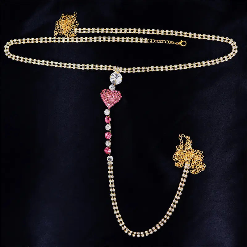 A sparkling gold heart rhinestone panty body jewelry featuring a pink rhinestone heart pendant with dangling crystals and ornate golden floral clasps for use as a garter belt.