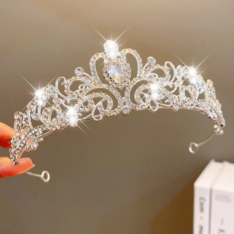A sparkling silver crown headband from sweet fashion jewelry featuring intricate lace-like patterns and numerous clear crystals with a central teardrop-shaped gemstone hair accessory.
