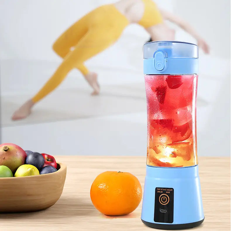 Light blue portable electric fruit juicer with transparent body filled with red and orange fruit chunks and ice for USB rechargeable mixing.