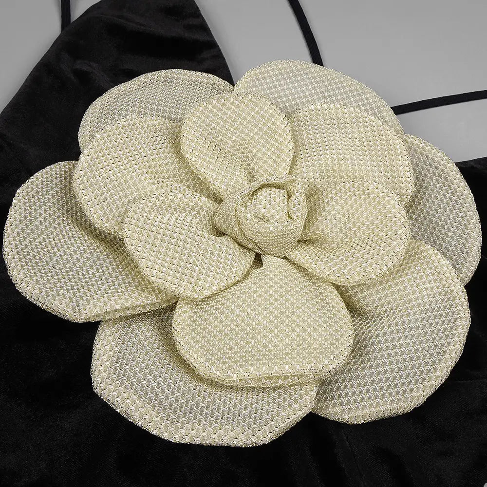a cream-colored textured fabric flower accessory with a woven pattern and layered petals on a black camisole backless slim fit velvet floral gown