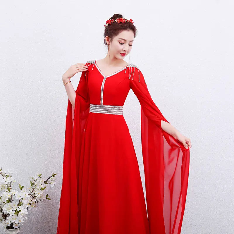 Elegant red long guzheng performance dress featuring a vibrant red gown with a v-neckline, flowing cape sleeves, and sparkling silver embellishments along the shoulders and waistband.