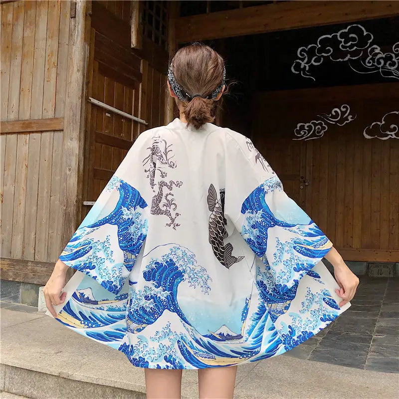 white kimono-style jacket featuring a vibrant blue wave and fish design inspired by hokusai the great wave off kanagawa with black ink detailing on the back, designed as sun protection clothing.
