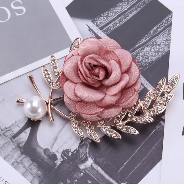 a delicate fabric flower lady temperamental pin featuring a soft pink fabric flower, gold-toned metal leaves with clear crystal accents, and a pearl detail in a floral brooch design