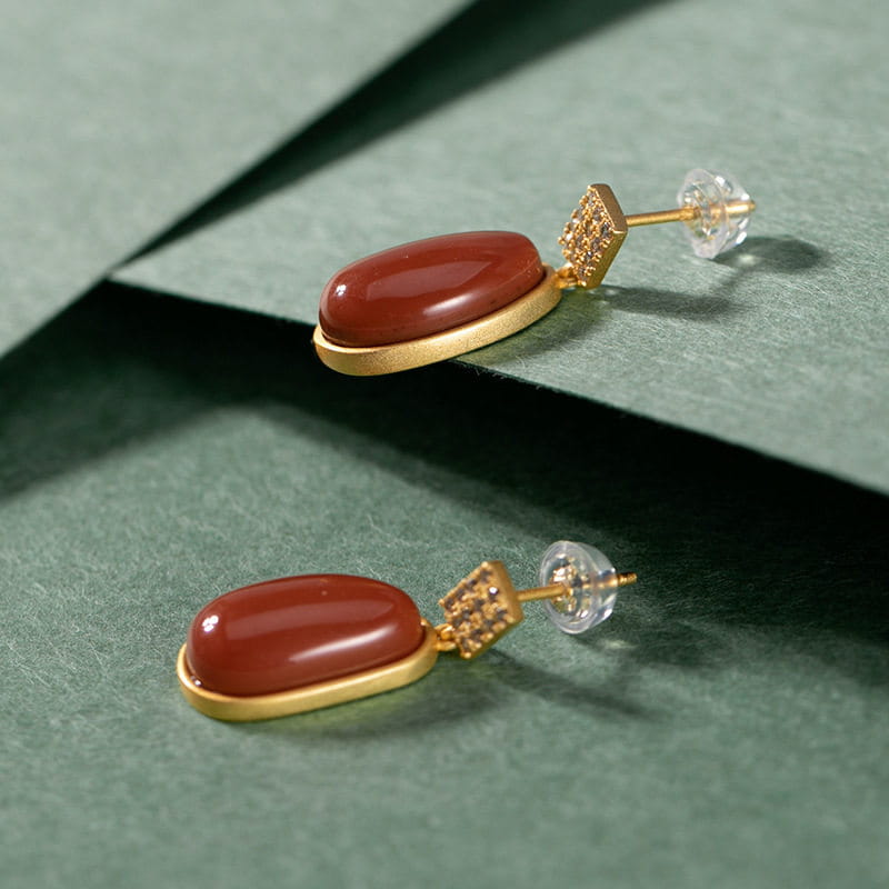 elegant southern red agate lucky bean earrings featuring red carnelian oval stones set in gold-toned metal with a small diamond-encrusted square accent.