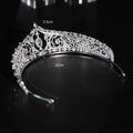 A silver filigree bridal crown with intricate patterns, embedded crystals, and a central oval gemstone for wedding makeup