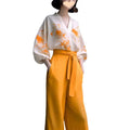 A woman wears a floral silk slimming white blouse with orange embroidery and a flab hiding shirt set in mustard yellow