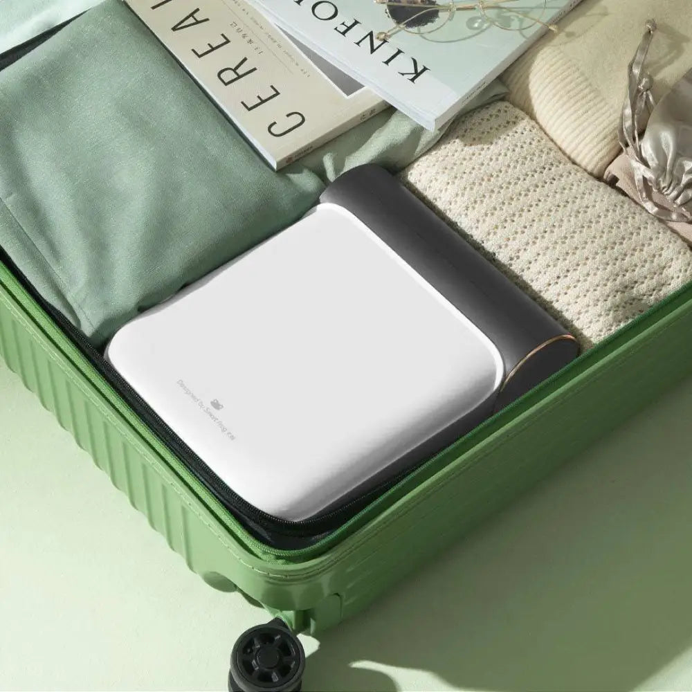 White and black portable travel charger with sleek minimalist design in green suitcase next to gray fabric small quick dryer