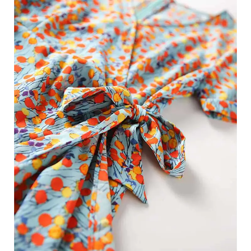 A light blue french floral slim polka dot wrap dress with vibrant orange yellow and purple blossoms tied at the waist